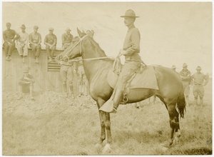 Soldater samlet seg og så på en uniformert soldat til hest på et gressfelt